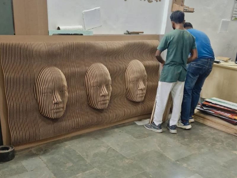 Parametric wall panel of stacked CNC cut ribs with three faces standing against the wall as the Dream3 team assembles it in Bijwasan